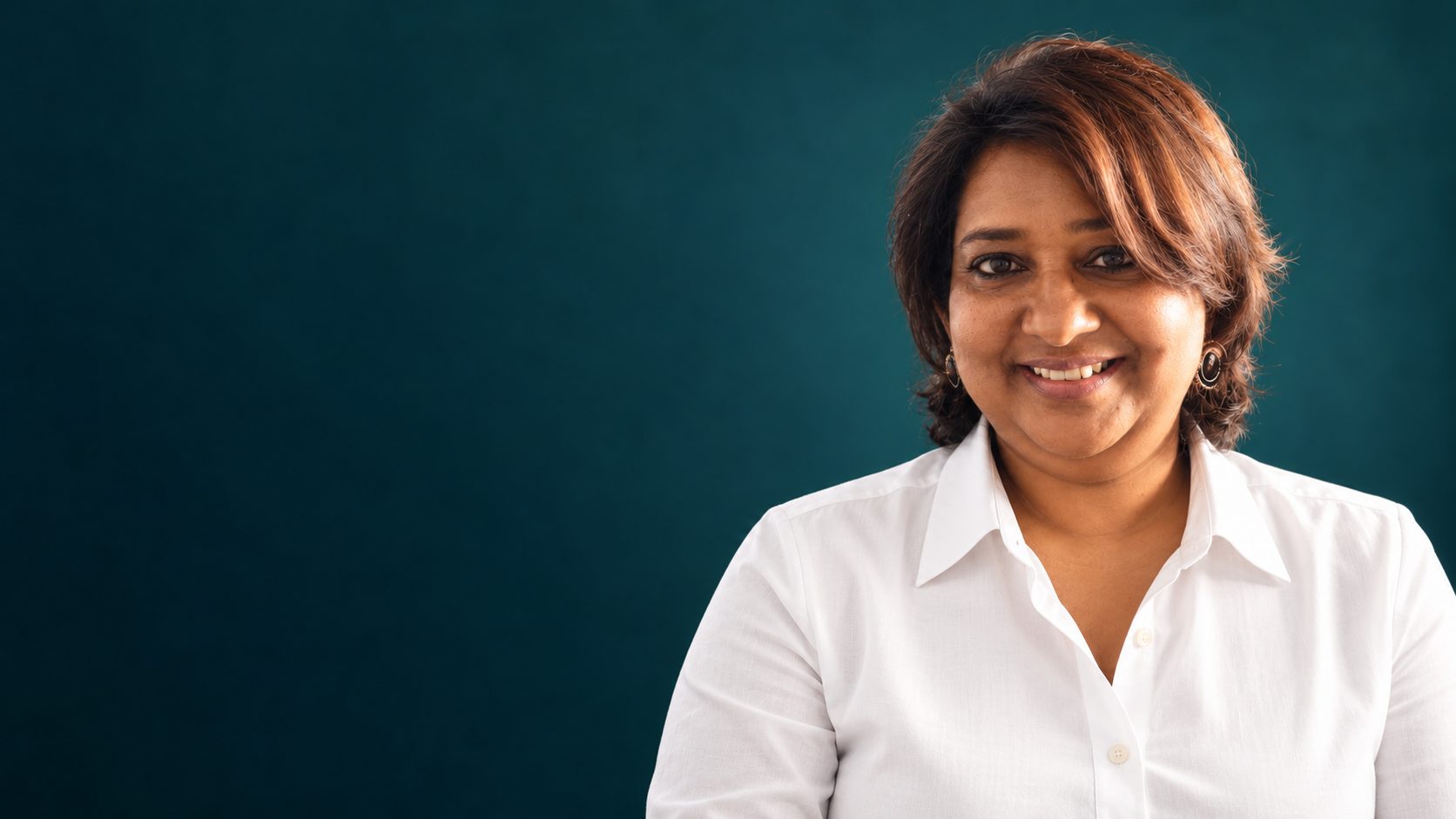 Iranthi Abeyasinghe smiling in a white shirt against a deep teal background